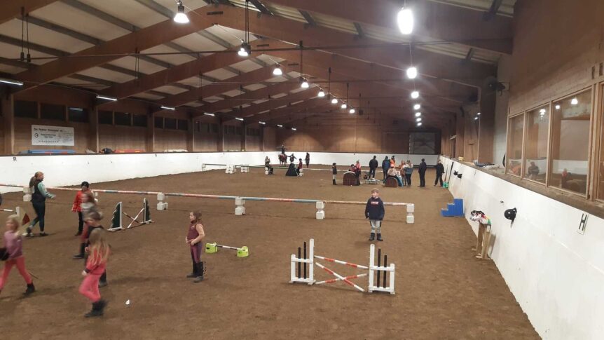 Rideskoleaktiviteter i innendørs ridehall med barn og voksne, hinder og treningsutstyr.