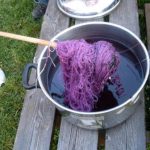 Lilla garn farges i en kjele utendørs, plassert på trebenk. En trepinne holder garnet oppe.