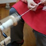Person spinner garn med en håndsnelle, iført rød forkle.