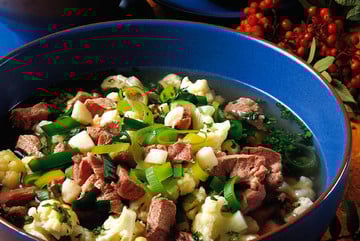 Tradisjonell norsk fårikål med kål, lammekjøtt og krydder servert i blå skål. Dekorert med rognebærkvister.