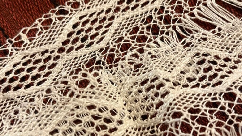 Håndlaget hvit blonder med intrikate mønstre på en brun bakgrunn.