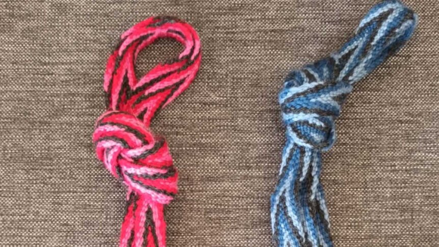 Fargerike bånd med flettede knuter på grå bakgrunn, en rød-hvit og en blå-hvit.