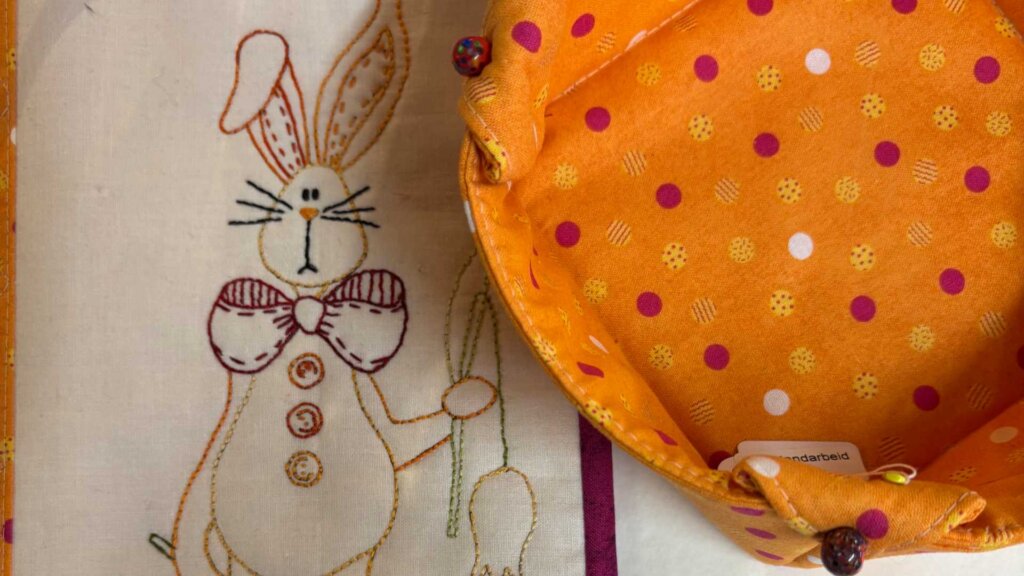 Fargerik tekstilkurv med prikker, ved siden av en brodert kaninfigur på lyst stoff.