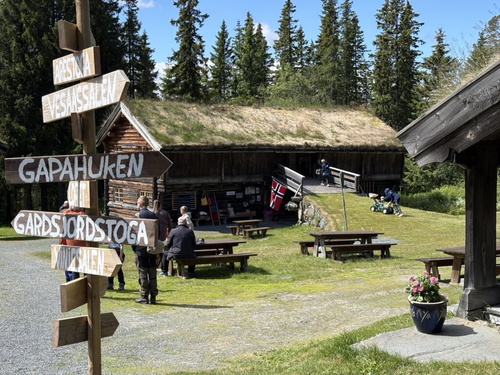 Klassisk norsk hytte med informasjonsskilt, mennesker, og barn som leker i vakker natur.