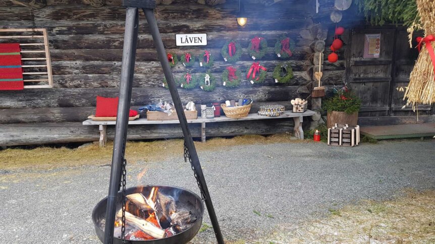 Bålsted foran en hytte med julekranser, håndverk og dekorasjoner. Koselig atmosfære med naturlige elementer.