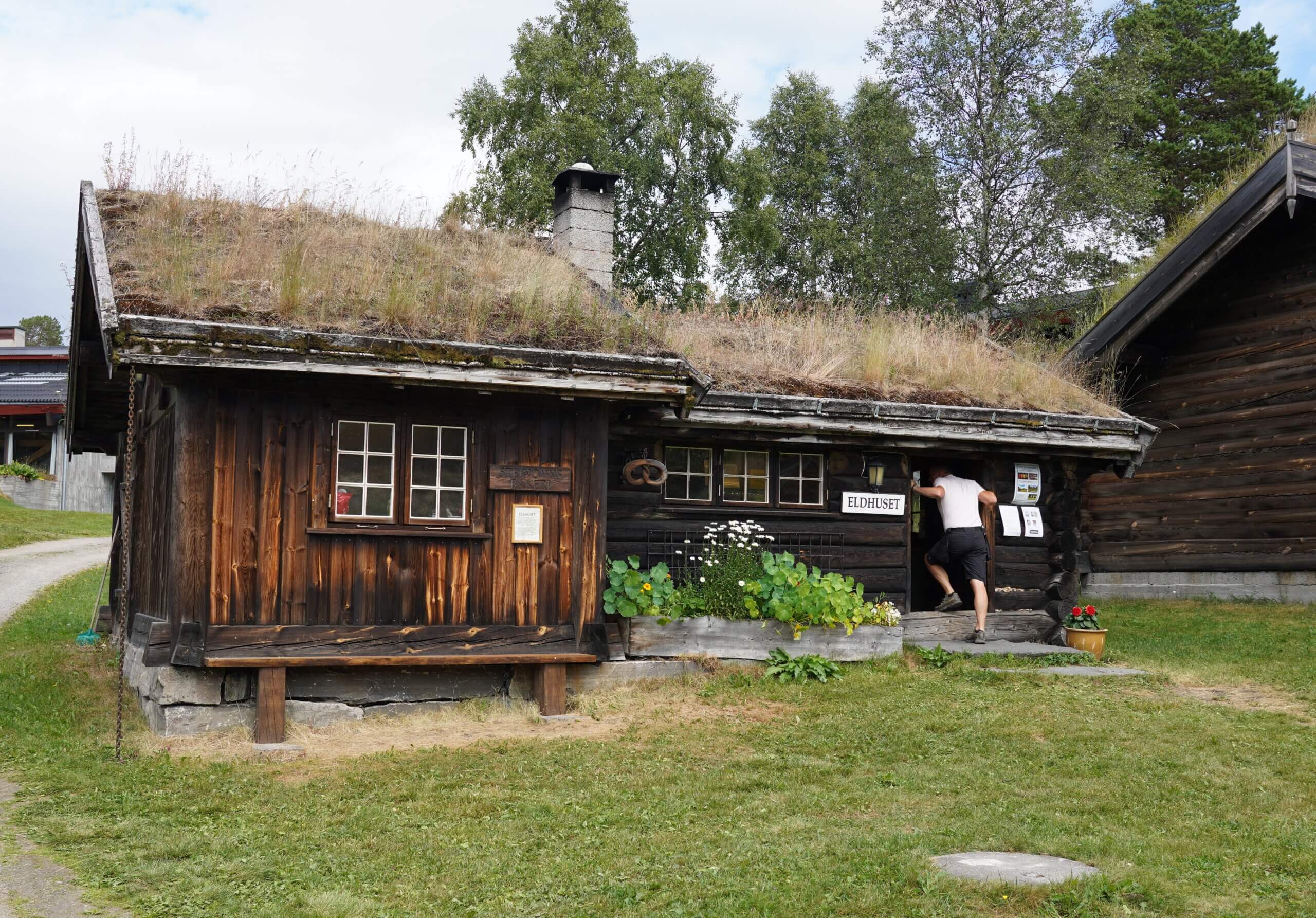 Eldhuset med torvtak, omkranset av grønne planter, gir en koselig atmosfære i naturskjønne omgivelser.