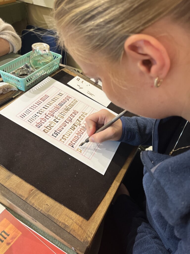 Ung kvinne skriver med pen på papir med kalligrafi, mens hun øver på bokstaver i en kreativ klasse.
