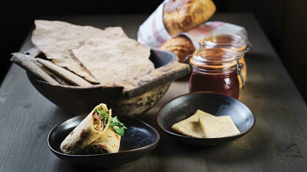 Autentisk norsk flatbrød og lefse servert med spekemat og ferske urter på trebord.
