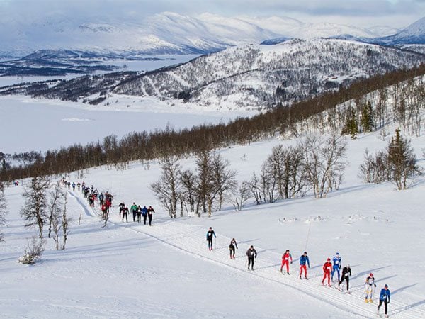 Langrennsløpere i fjellterreng med snødekte landskap i bakgrunnen under en vinterdag.