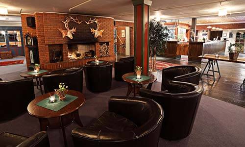 Koselig hotellobby med peis, skinnstoler og dekorative hjortehoder på murveggen.