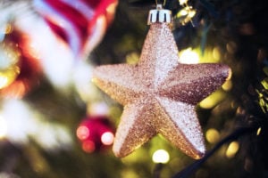 Gullstjerne julepynt på juletre, glitrende med vinterlys i bakgrunnen.