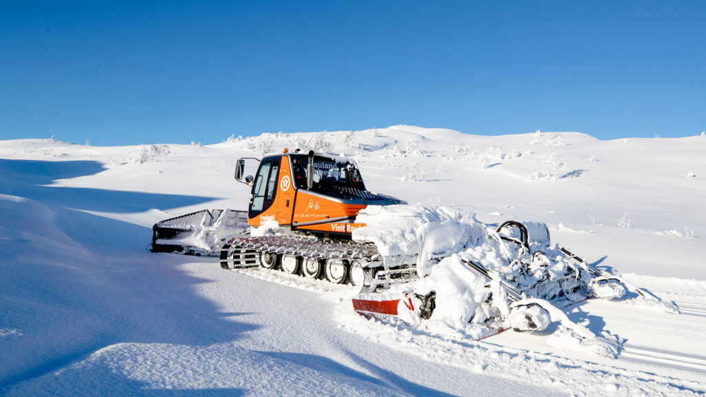 Snøplog i bruk i snødekt landskap under klar blå himmel i Rauland, Norge.