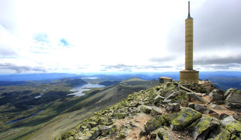 Utsikt fra Gaustatoppen med telekommunikasjonstårn og fjellandskap i bakgrunnen, klart vær og imponerende natur.
