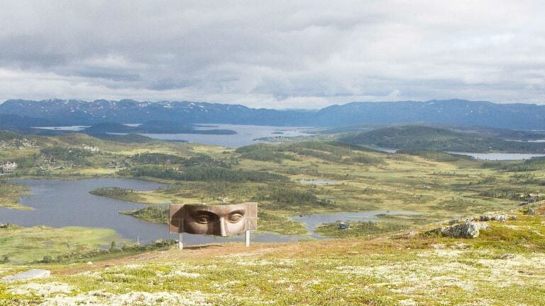 Panoramautsikt over fjellandskap med kunstinstallasjon i forgrunnen, fjell og innsjøer i bakgrunnen.
