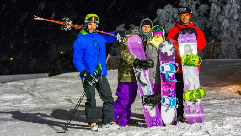 Gruppe snowboardere og skiløper i fargerike klær på snødekt nattbakke.