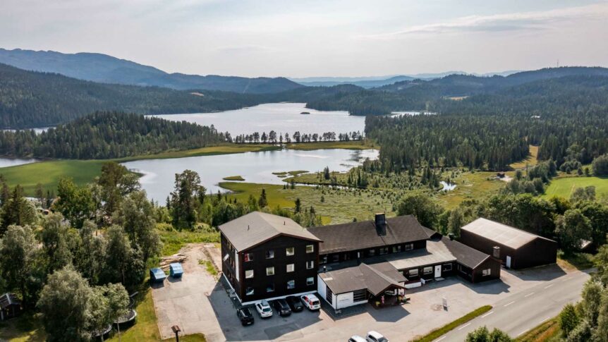 Hotel ved innsjø omgitt av skog og fjell i Norge, fredelig natur med parkerte biler foran bygningen.