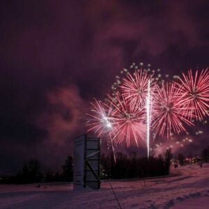 Fyrverkeri lyser opp nattehimmelen over et snødekt landskap, feststemning i luften.