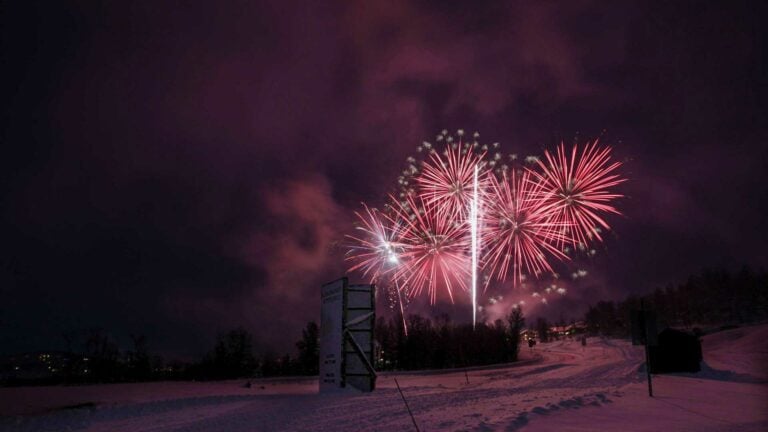 Fyrverkeri lyser opp nattehimmelen over et snødekt landskap, feststemning i luften.