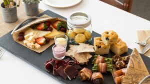 Delikatessefat med ost, frukt, poteter, kjeks, kjøtt og bakevarer på et svart brett. Perfekt for sammenkomster.