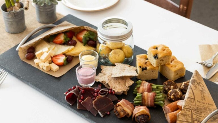 Delikatessefat med ost, frukt, poteter, kjeks, kjøtt og bakevarer på et svart brett. Perfekt for sammenkomster.