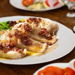 Tallerken med stekt fisk, erter og bacon, servert med salat og sitron på trebord.