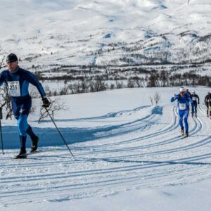 Langrennsløpere i konkurranse på snødekte fjell, med dramatiske vinterlandskap i bakgrunnen.