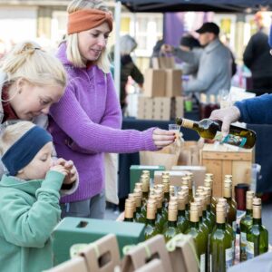 Familie smaker olivenolje på utendørs marked, flasker på bordet.