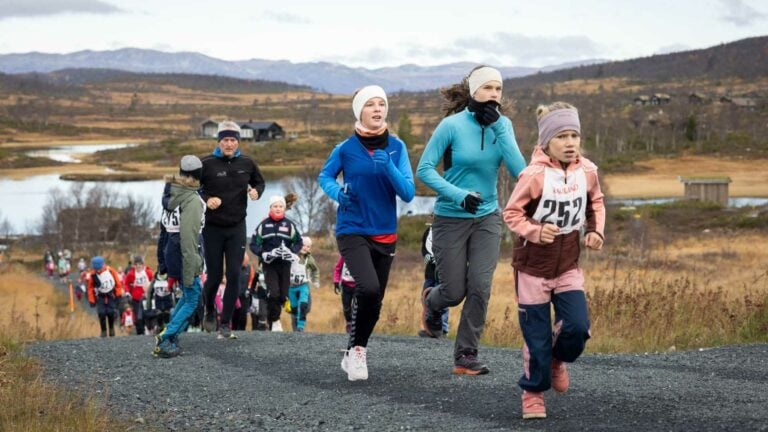 Løpere deltar i et terrengløp i vakker natur med fjell og innsjø i bakgrunnen.