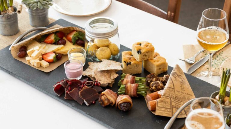 Tapasbrett med ost, frukt, brød, kjøtt og dipp servert med ølglass på borddekking.