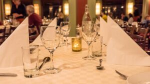 Pent dekket restaurantbord med vinglass, tøyservietter og levende lys.