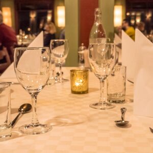 Pent dekket restaurantbord med vinglass, tøyservietter og levende lys.