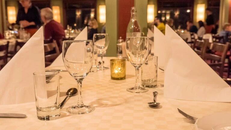Pent dekket restaurantbord med vinglass, tøyservietter og levende lys.