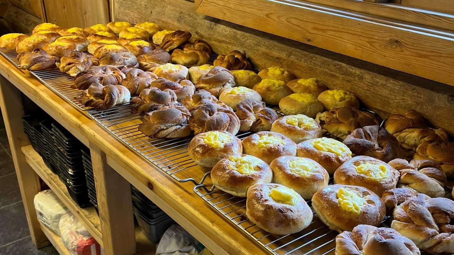 Ferske boller og bakverk på en trehylle i bakeri. Perfekt for frokost eller kaffepause.