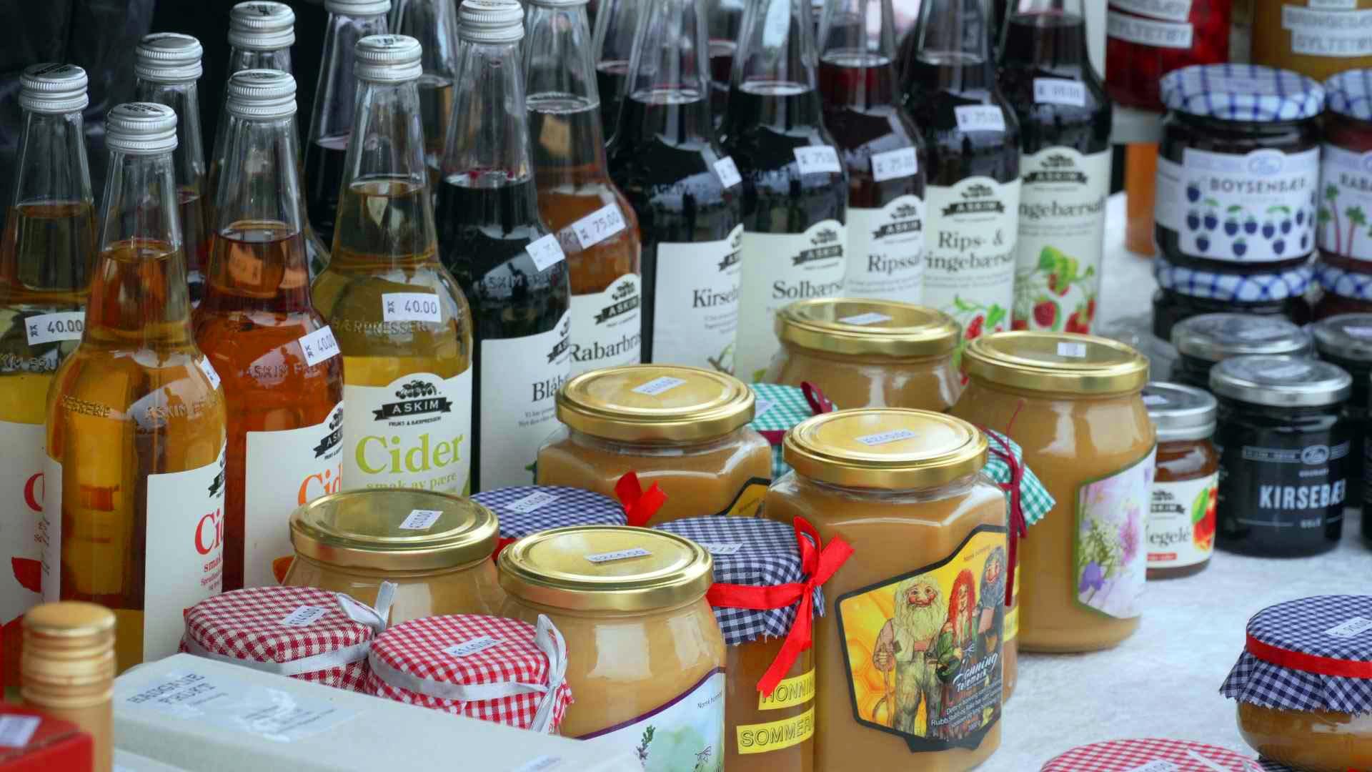 Flasker med cider og syltetøyglass utstilt på et marked, diverse smaker og varianter.