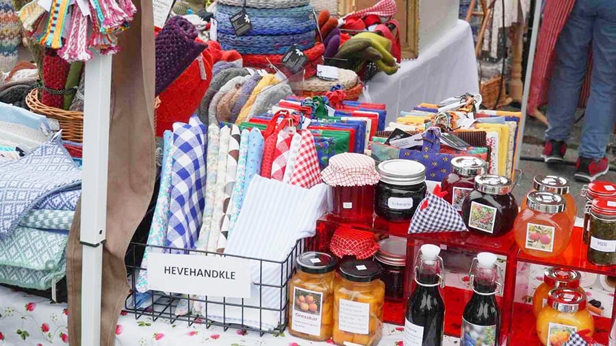 Markedbod med håndlagde produkter som tekstiler, syltetøy og krydder. Fargerike og hjemmelagde varer til salgs.