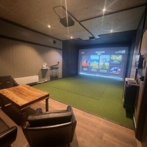Indoor golfsimulator med storskjerm, kunstgress og sittegruppe i en moderne, stilfullt innredet stue.