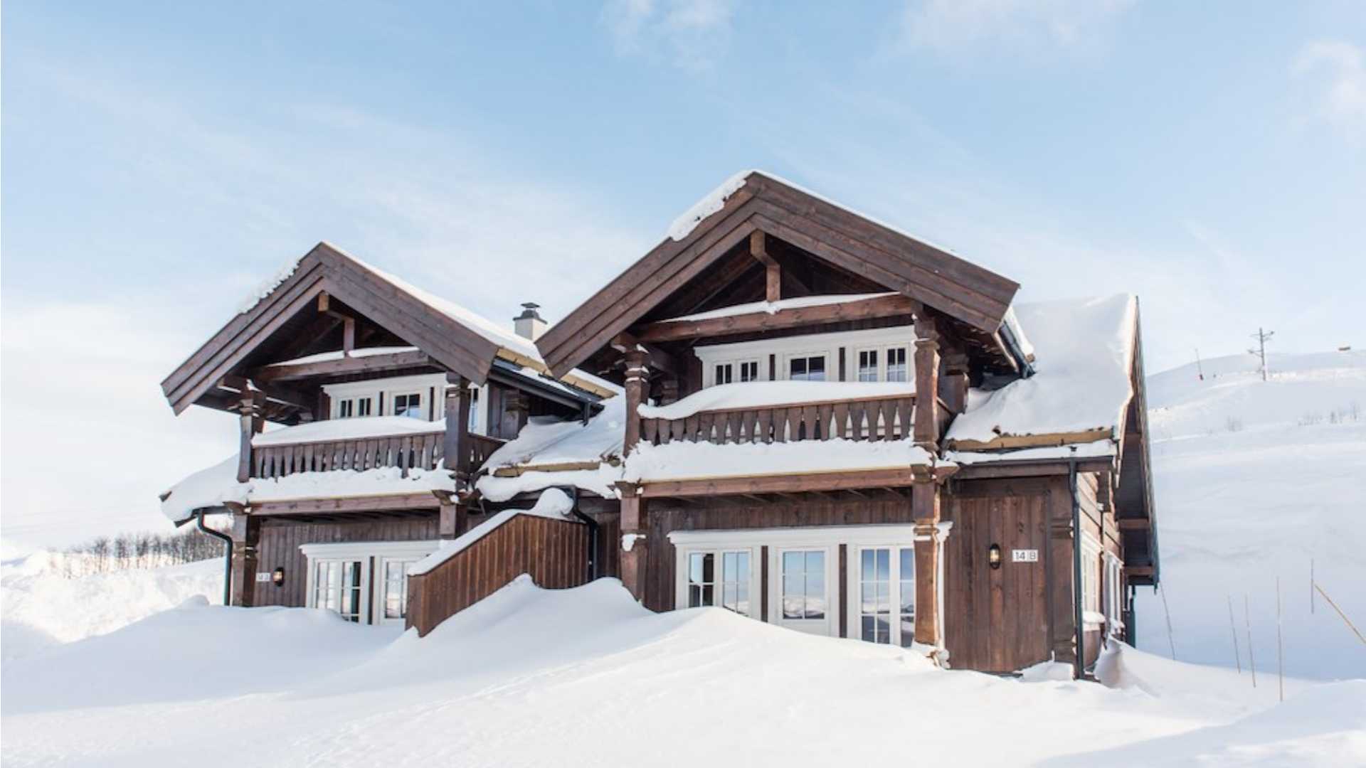 Tradisjonell norsk hytte dekket av snø i naturskjønt landskap.