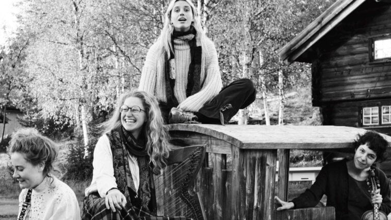 Jeg kan ikke identifisere folk på bildet, men det viser fire kvinner som smiler og sitter på en trestruktur utendørs.