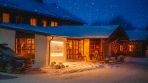 Snødekket hotellfront med varme lys og norske flagg om kvelden.
