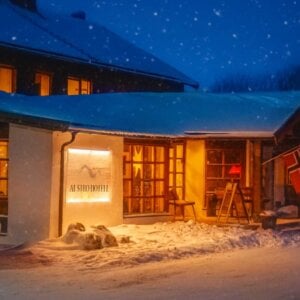 Snødekket hotellfront med varme lys og norske flagg om kvelden.