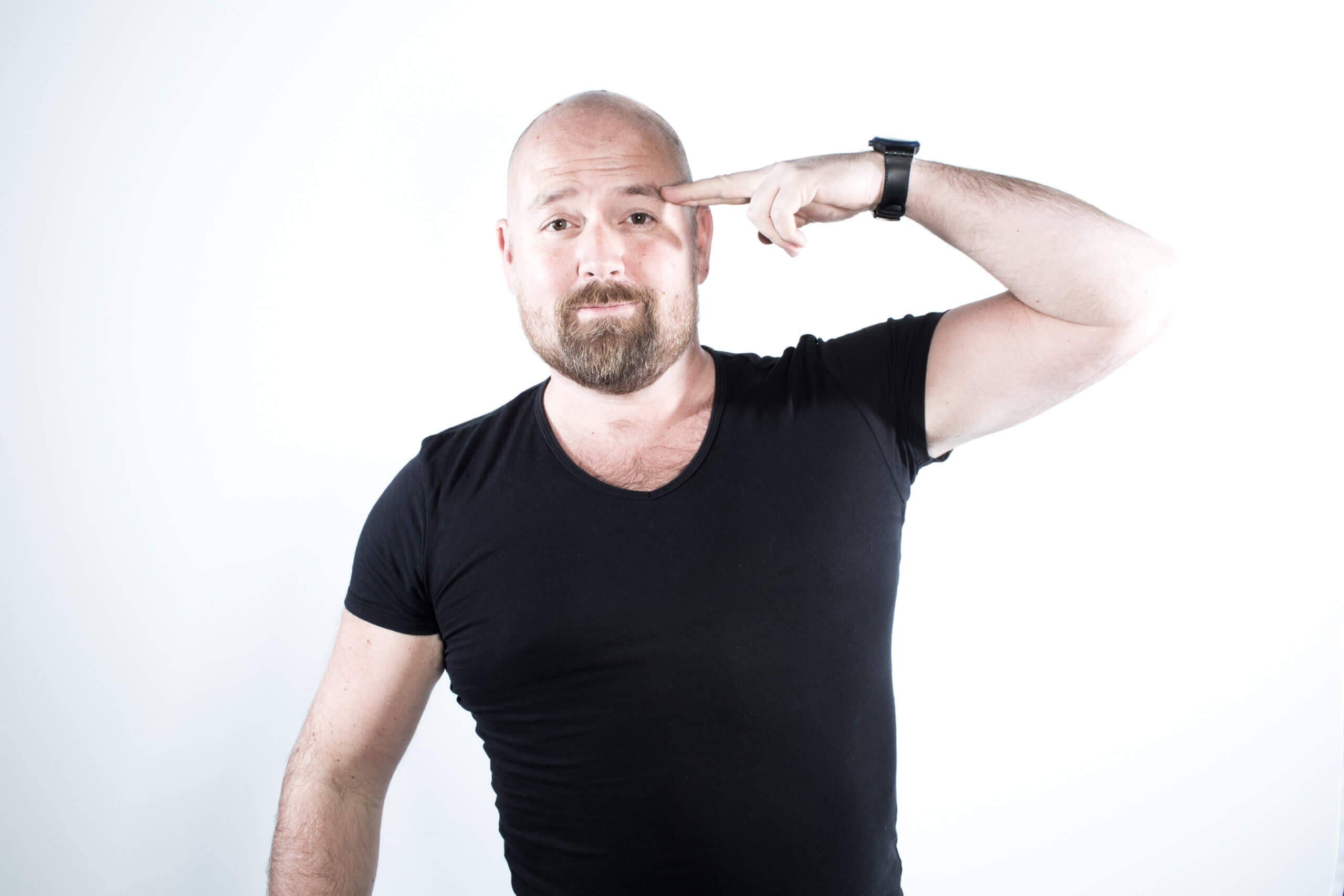 En mann i svart t-skjorte peker mot hodet med fingeren, uttrykker tankefullhet.