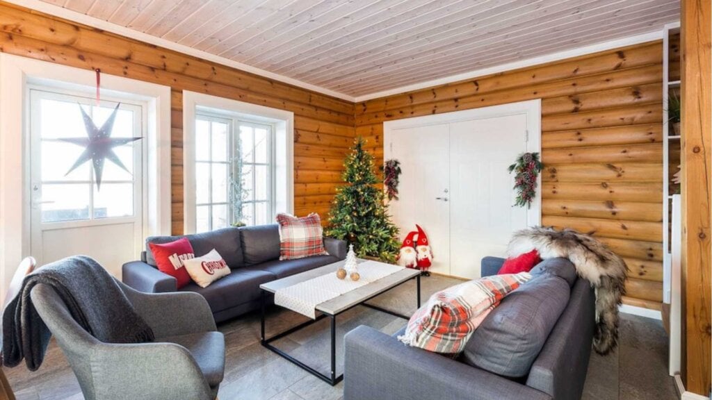 Koselig stue med julepynt, juletre, sofa og pute. Hytteinteriør med trevegger og moderne sitteplasser.