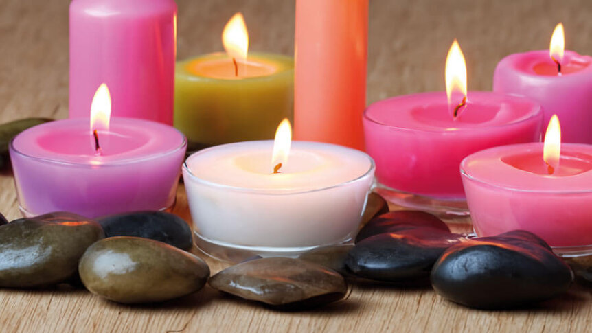 Fargerike telys og stearinlys blant glatte steiner på trebord, skaper en avslappende atmosfære.