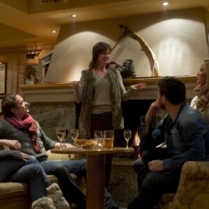 Gruppe venner samlet foran peis, prater og nyter drikke i koselig stue.