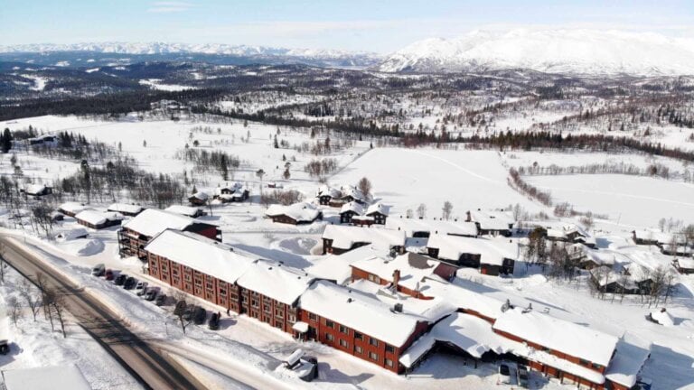 Vinterlandskap med snødekte hus og fjell i bakgrunnen. Perfekt for naturopplevelser og vinteraktiviteter.