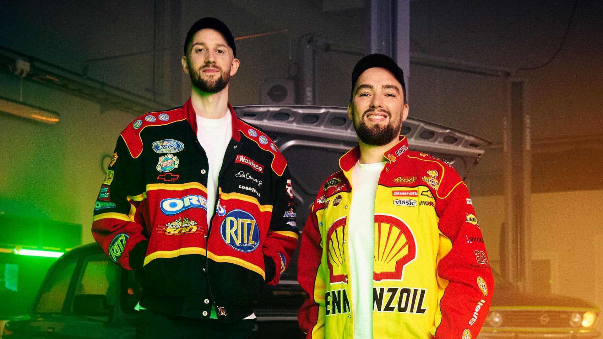 To personer i fargerike racingjakker står foran en bil i en garasje.