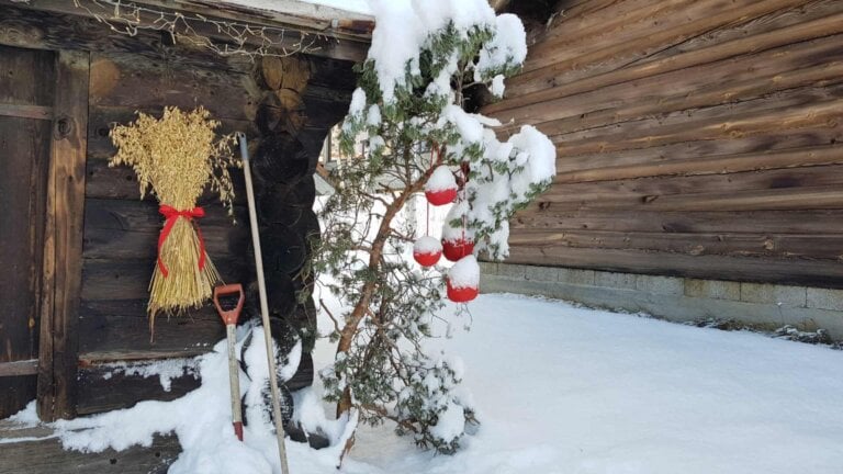 Tradisjonell jul dekorasjon med røde bøtter og en bunt halm ved trevegg i snødekt landskap.