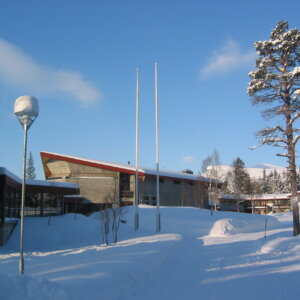 Moderne bygning omgitt av snø og vinterlandskap, klar blå himmel, trær med snø.