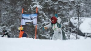 Person i tradisjonell drakt med ski, deltar i konkurranse i snødekte fjellskog.