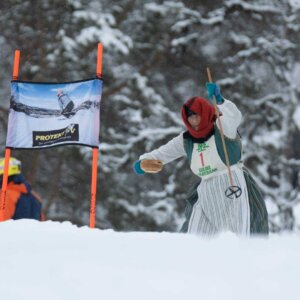 Person i tradisjonell drakt med ski, deltar i konkurranse i snødekte fjellskog.